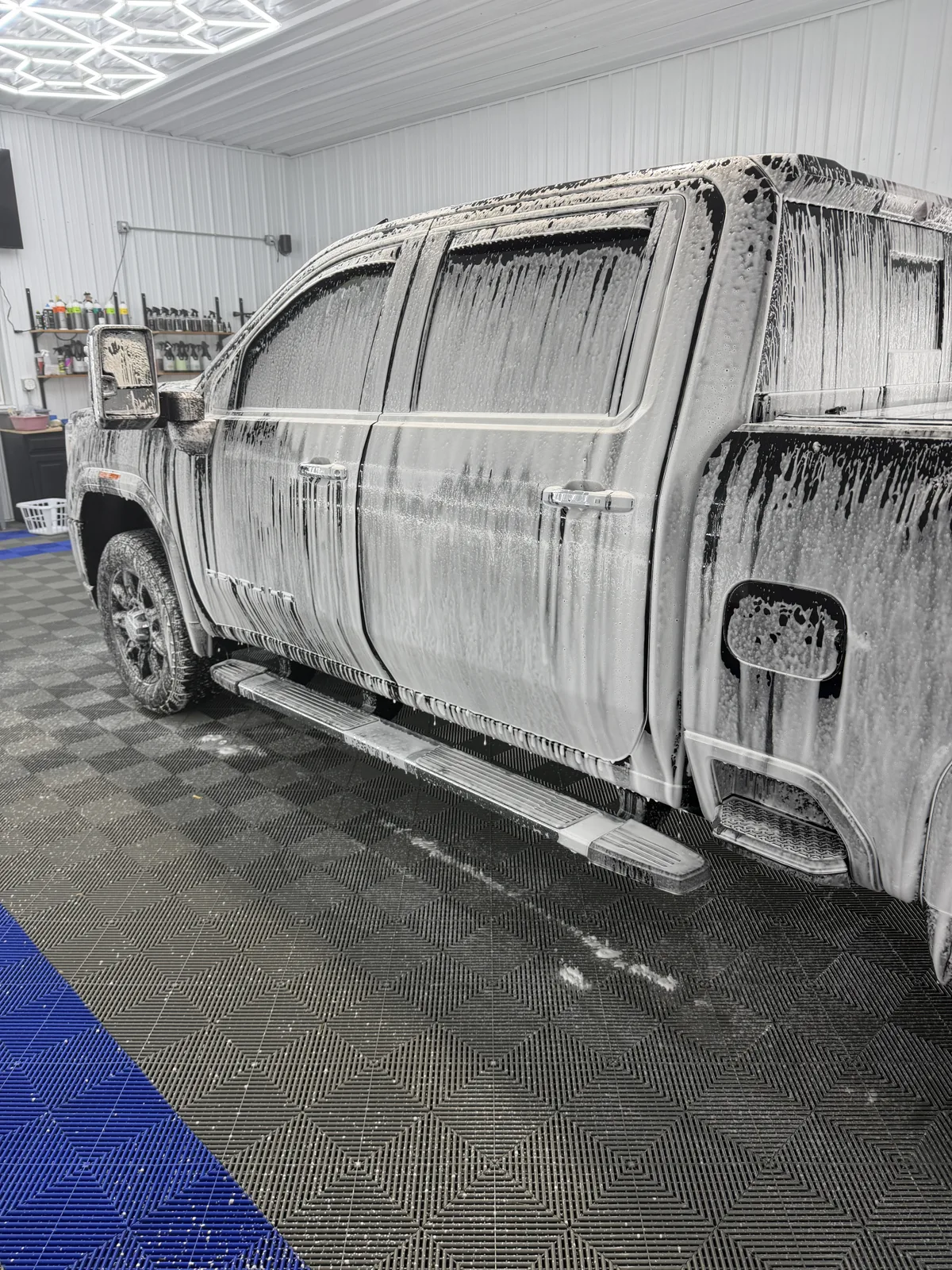 Dark pickup truck covered in thick foam during a maintenance wash inside the Porter’s Detailing bay
